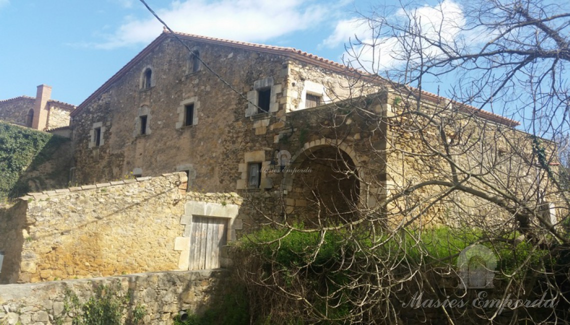 Fachada principal de la masía con pasaje de calle a través de arco de medio punto