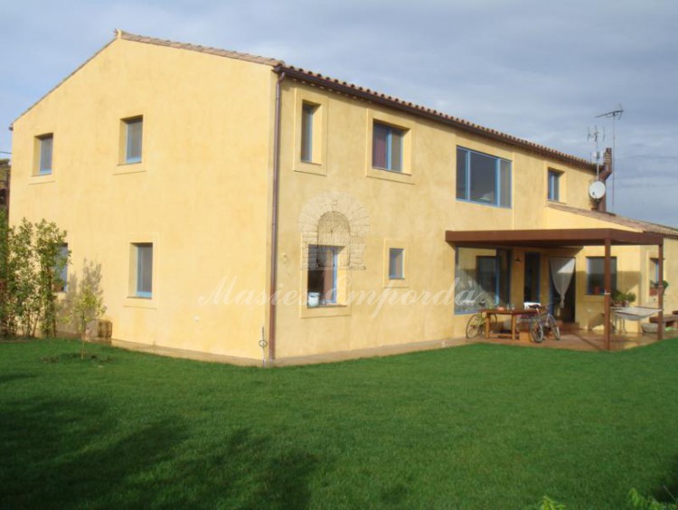 Vista de la casa desde el jardín de la propiedad donde destaca el porche avanzado como terraza con vistas a Pals de Empordà